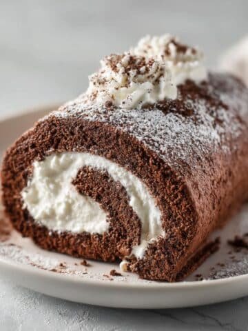 Homemade Swiss cake roll slice filled with cream, dusted with powdered sugar on a white plate — natural lighting, top-down shot.