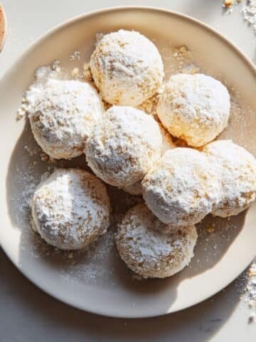 Vegan Russian tea cakes dusted with powdered sugar cooling on a rack on a white kitchen counter.