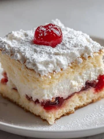 A homemade heaven on earth cake slice with creamy layers of pudding, cherries, and whipped topping on a white plate.
